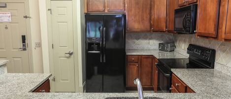 Una cocina con encimeras de granito, refrigerador de acero inoxidable, gabinetes de madera, microondas y estufa.