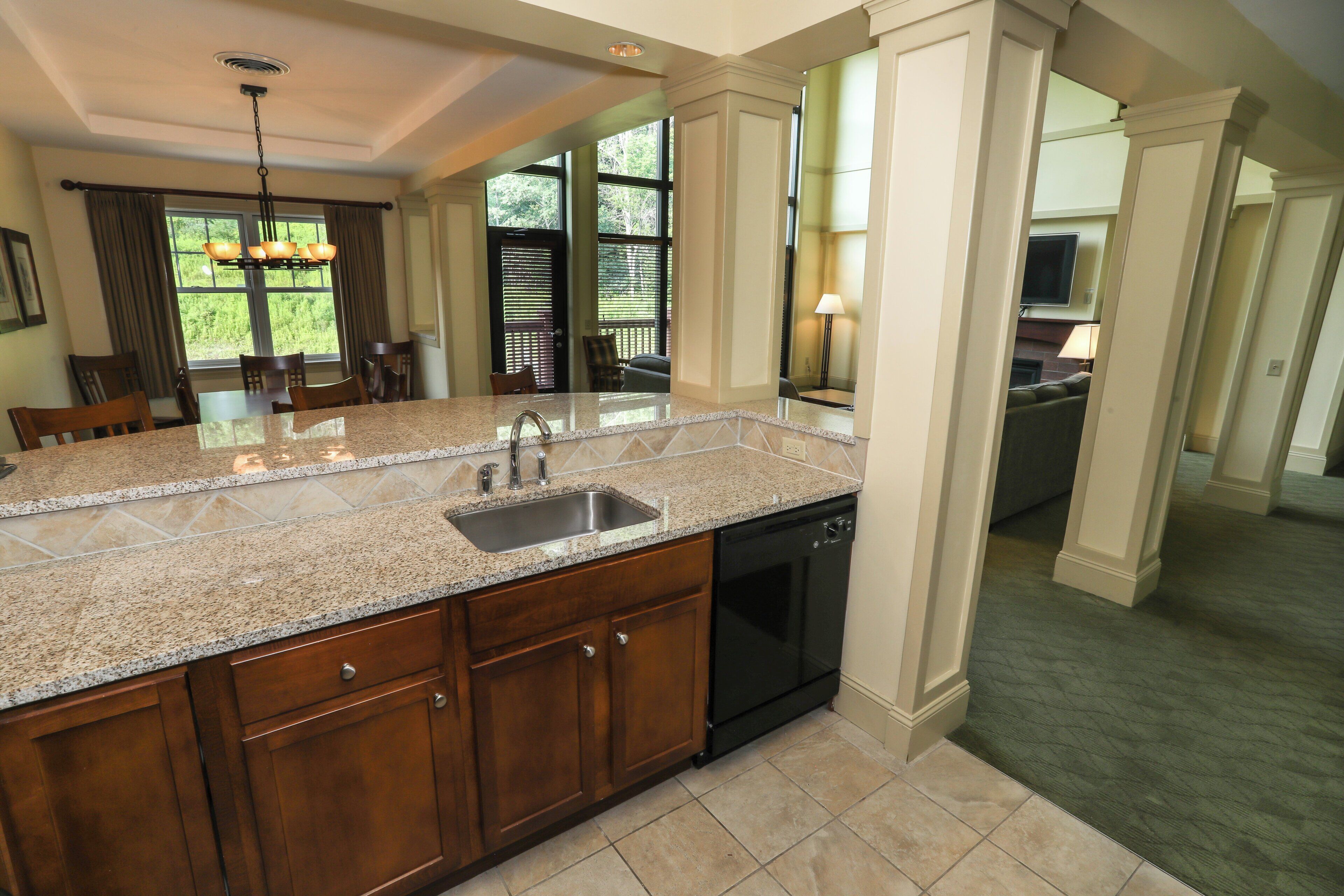 A kitchen with granite countertops, a sink, and a dishwasher. There is a dining area with a table and chairs.