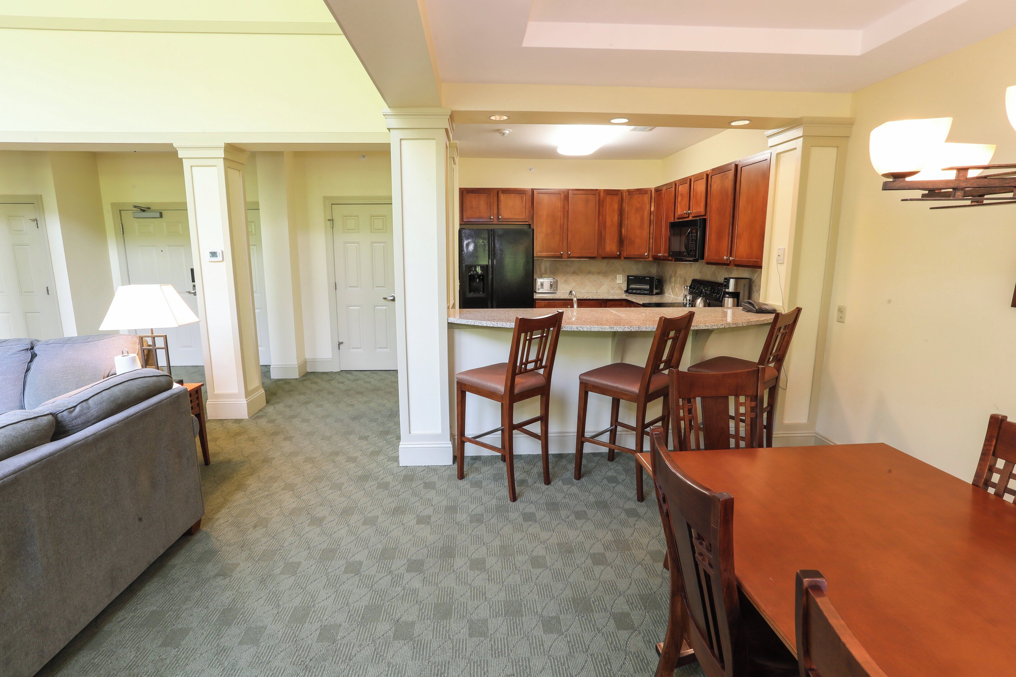 A spacious living room with a sofa, a dining table with chairs, and a kitchen area with wooden cabinets and appliances.