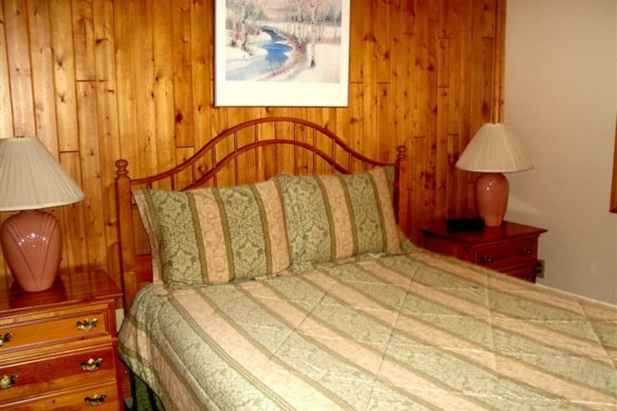 A wooden-paneled bedroom with a bed, two nightstands, and a painting on the wall.
