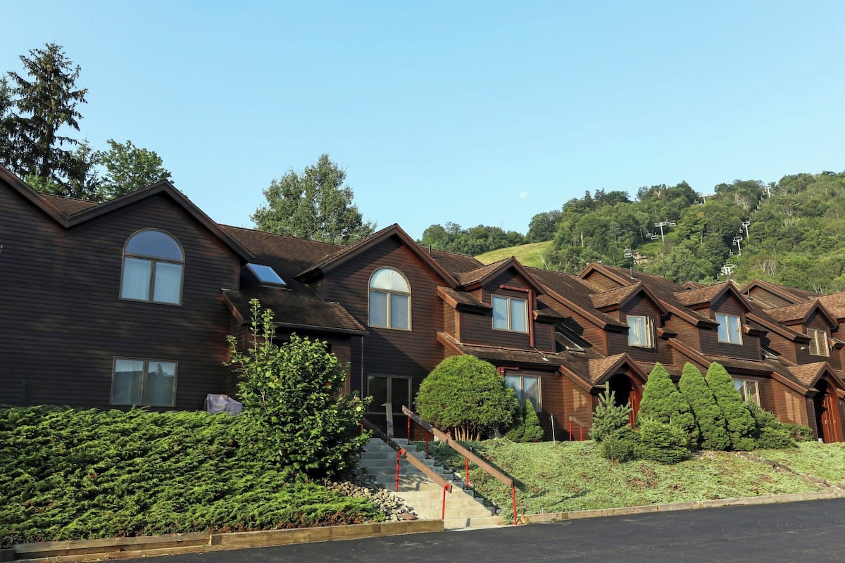 A row of wooden houses with a steep driveway and a small staircase leading to the entrance.