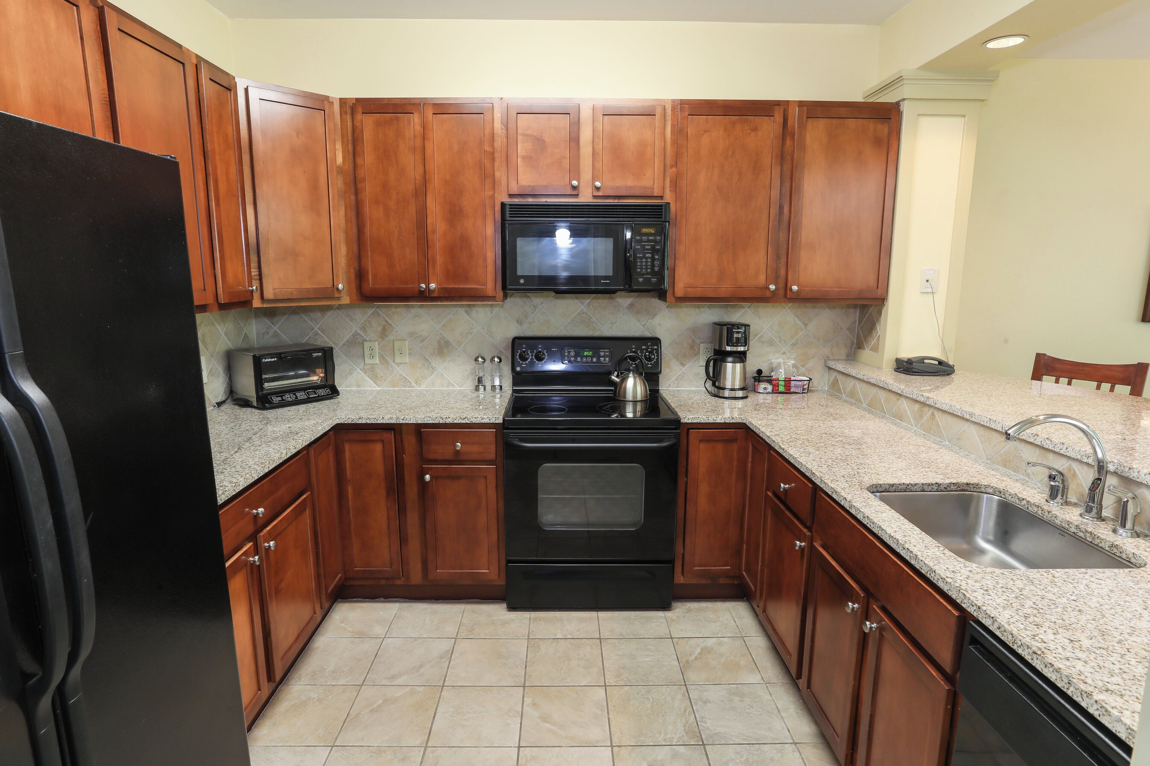 A kitchen with wooden cabinets, a black refrigerator, a microwave, a stove, and a sink.