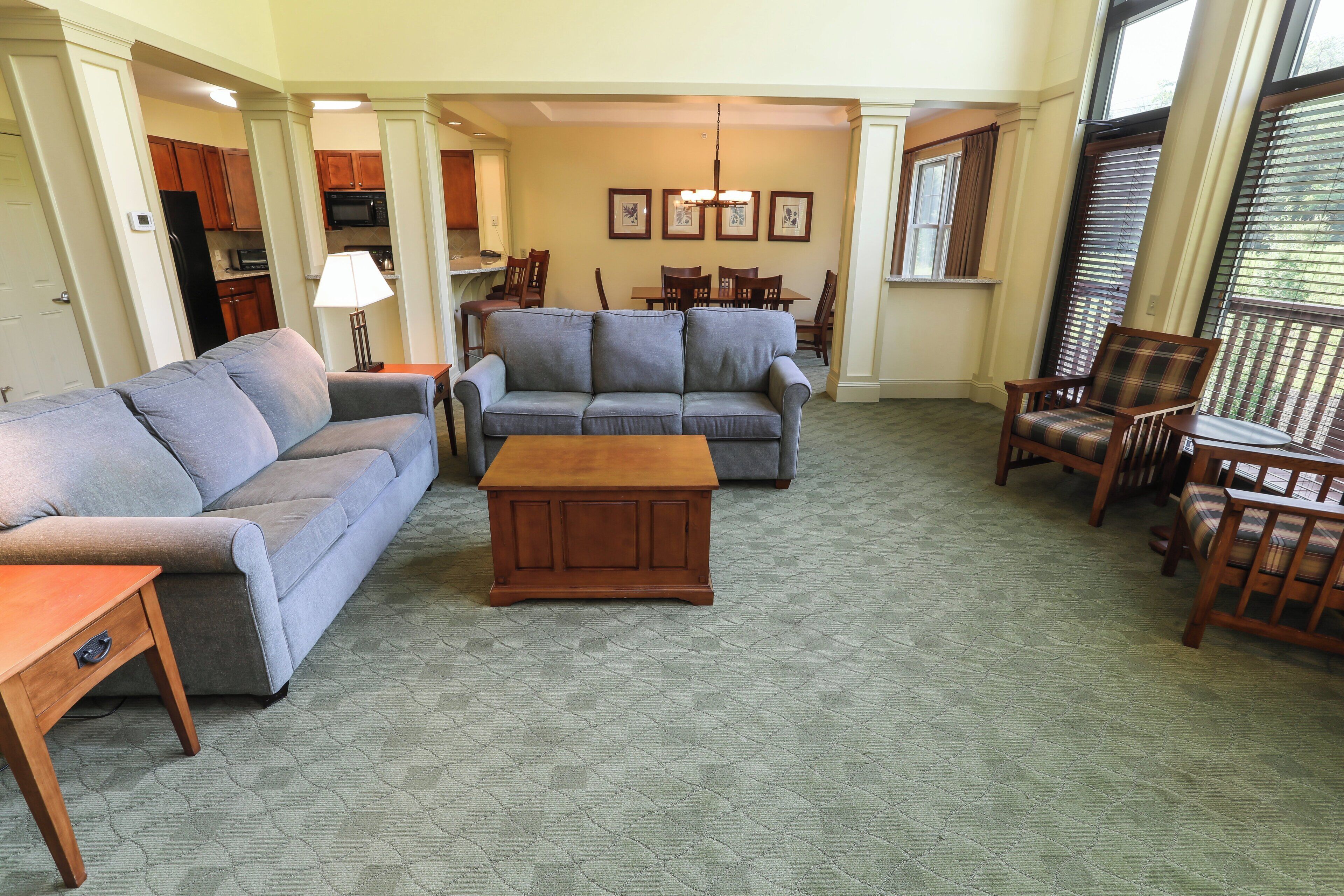 Una sala de estar con un sofá gris, una mesa de centro de madera, y un comedor con sillas y una mesa de madera.