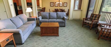 Una sala de estar con un sofá gris, una mesa de centro de madera, y un comedor con sillas y una mesa de madera.