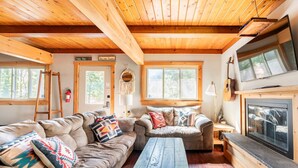 L’intérieur d’un chalet accueillant, avec un plafond en bois, deux canapés, une table basse, une cheminée et un téléviseur.
