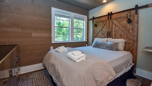 A bedroom with a wooden headboard, a large window, and a bed with towels. - Calming Seaside Sanctuary, pet friendly 2-blocks from beach (Galveston)