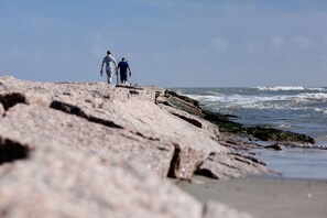 Two people walking on a rocky shoreline with waves crashing nearby.