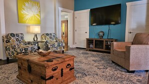 A living room with two patterned armchairs, a wooden chest, a television, and a blue accent wall. - Calming Seaside Sanctuary, pet friendly 2-blocks from beach (Galveston)