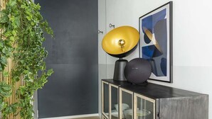 Un intérieur moderne avec une porte gris foncé, une lampe jaune et noire posée sur un meuble, et une œuvre d’art abstraite accrochée au mur.