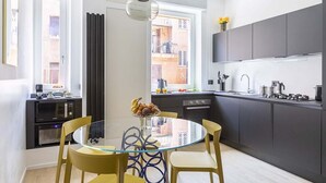 Une cuisine moderne avec des meubles de couleur sombre, une table à manger en verre et une vue sur la ville par la fenêtre.