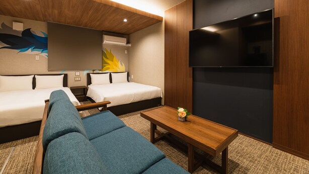 A modern hotel room with a large bed, a sofa, a small table, and a flat-screen TV mounted on the wall. - Grand Base Shianbashi (Nagasaki)