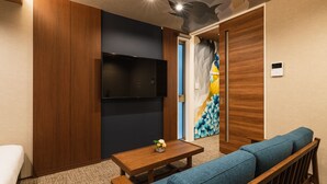 A modern living room with a wooden sofa, a small wooden table, and a flat-screen TV mounted on the wall. - Grand Base Shianbashi (Nagasaki)