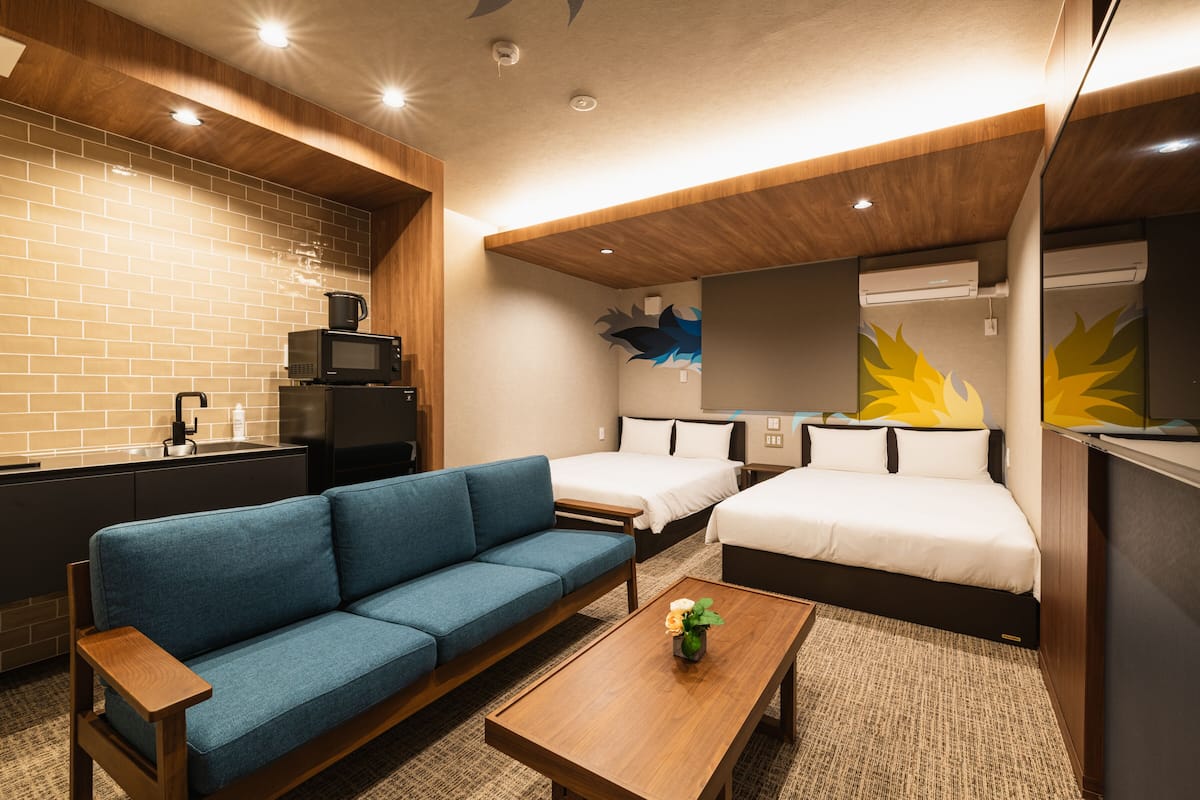 Une chambre d’hôtel moderne avec un canapé bleu, deux lits simples, une table basse en bois, un four à micro-ondes et un évier.