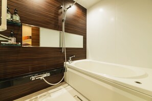 A modern bathroom with a wooden vanity, a large mirror, and a white bathtub. - Grand Base Shianbashi (Nagasaki)