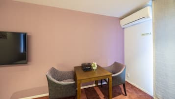 A small room with two grey armchairs, a wooden table, a flat-screen TV, and an air conditioning unit.