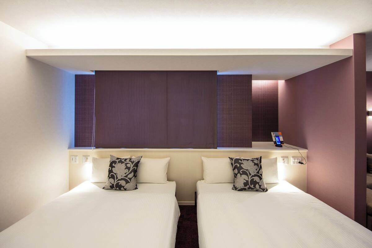 A hotel room with two beds, a small desk, and a mirror.