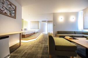 Quarto de hotel moderno com sofá, mesa de jantar, pequena cozinha e cama.