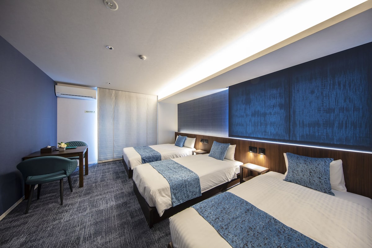 A hotel room with three beds, a desk, and a chair.