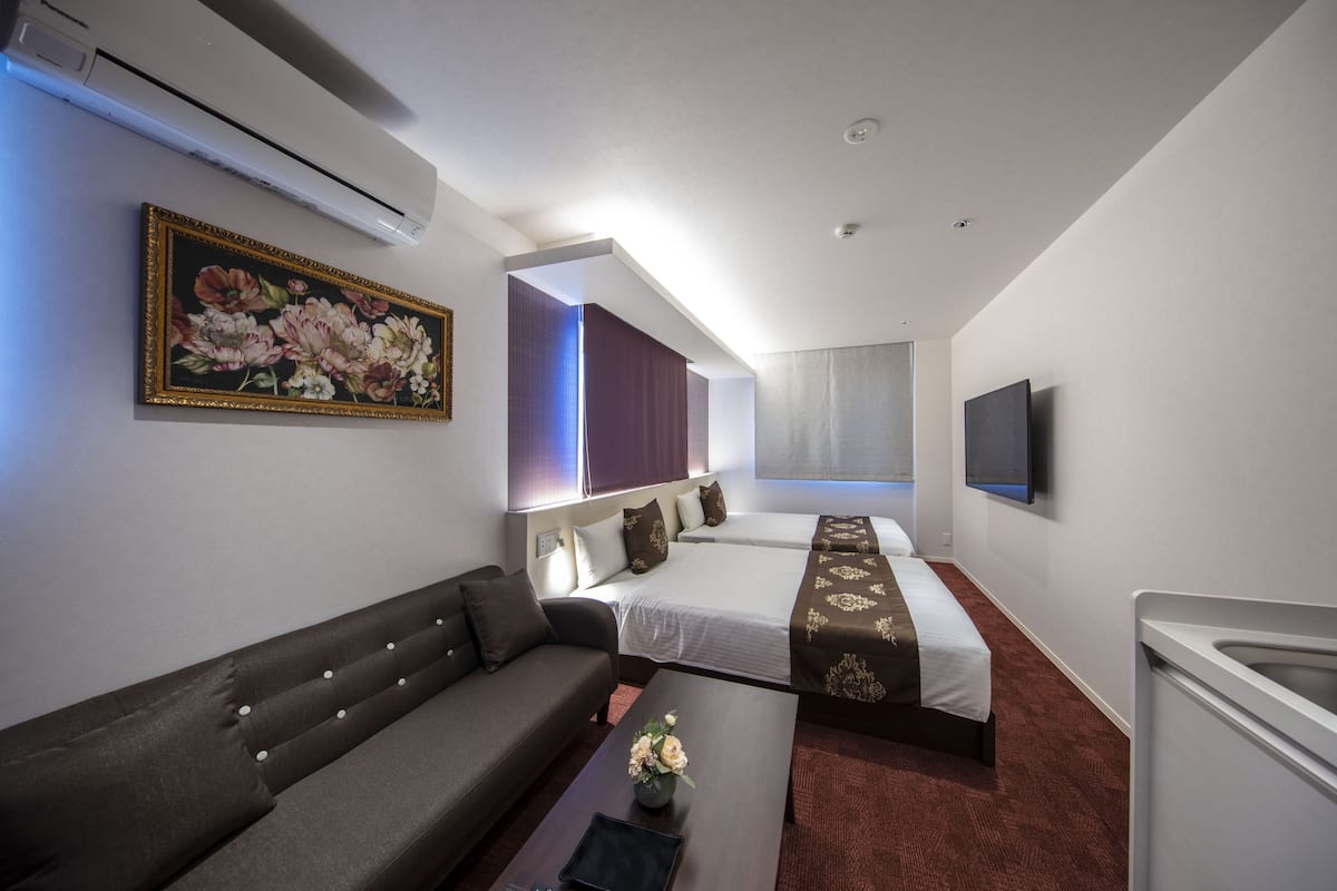 A hotel room with a sofa, a bed with a decorative headboard, a flat-screen TV, and a painting on the wall.