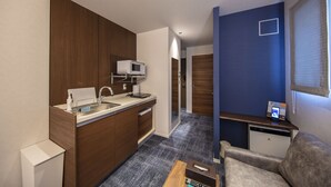 A compact hotel room with a kitchenette, a small seating area, and a view of the hallway. - Grand Base Okayama Ekimae (Okayama)