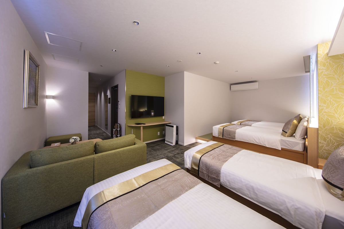 A hotel room with a sofa, two single beds, a TV, and a small desk.