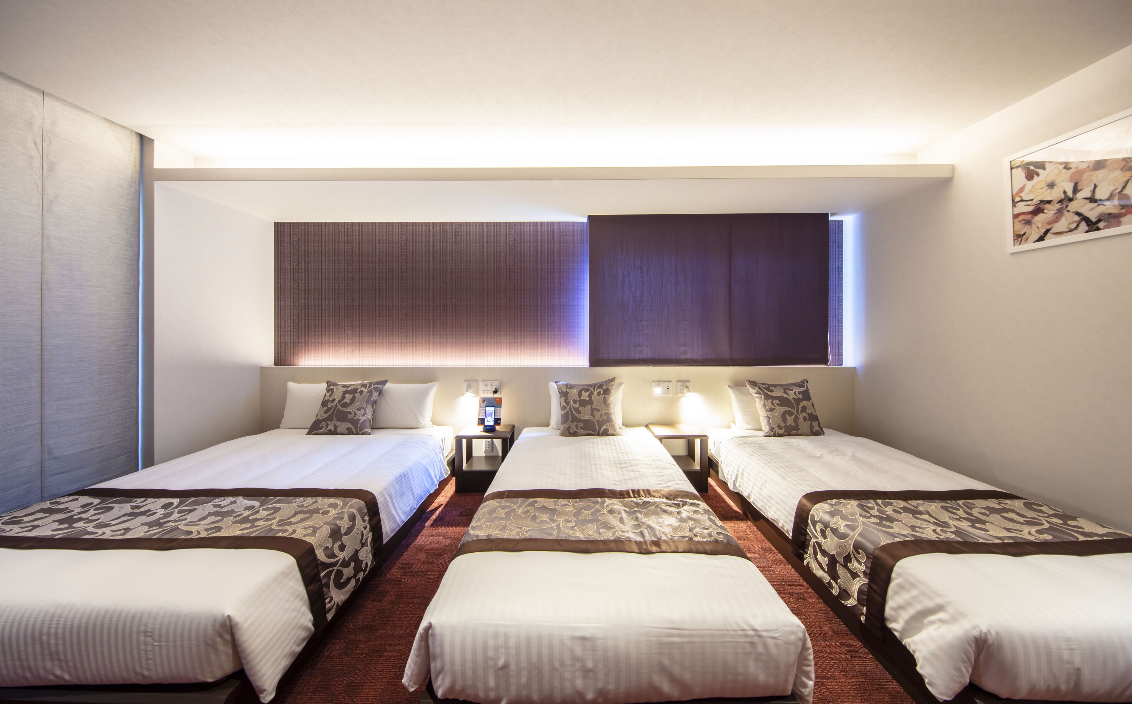 A hotel room with three single beds, a large window with blinds, and a painting on the wall.