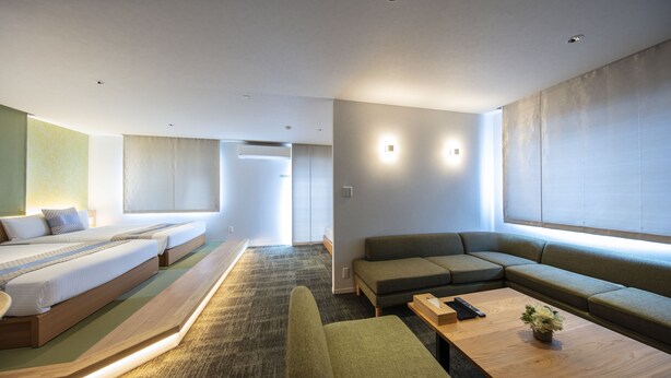 A hotel room with a bed, sofa, and a small table with a remote control and a flower vase. - Grand Base Okayama Ekimae (Okayama)