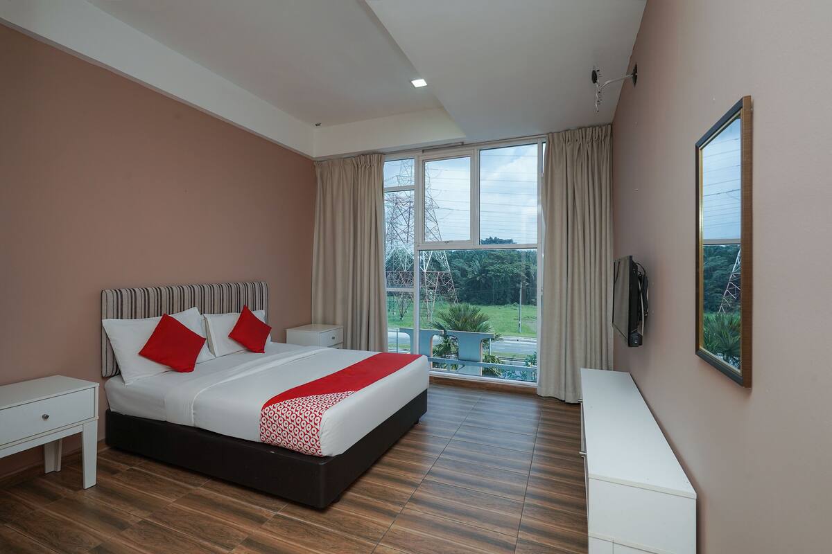 Ein Schlafzimmer mit einem großen Bett, einem Nachttisch, einer Kommode, einem Fernseher und einem Balkon mit Blick ins Grüne.