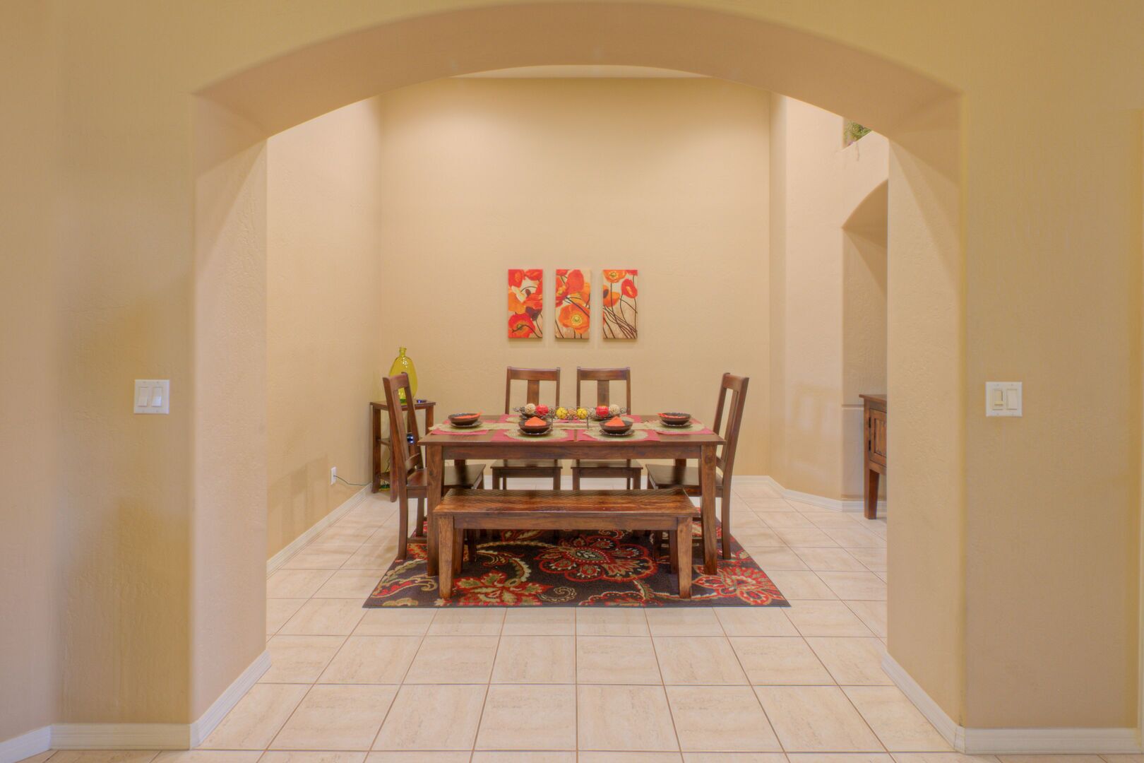 Un coin repas avec une table et des chaises en bois, un tapis à motifs et trois tableaux accrochés au mur.