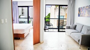 Ein modernes Hotelzimmer mit Bett, einer Couch, einem Essbereich mit Tisch und Stühlen sowie einem Balkon mit Blick ins Freie.