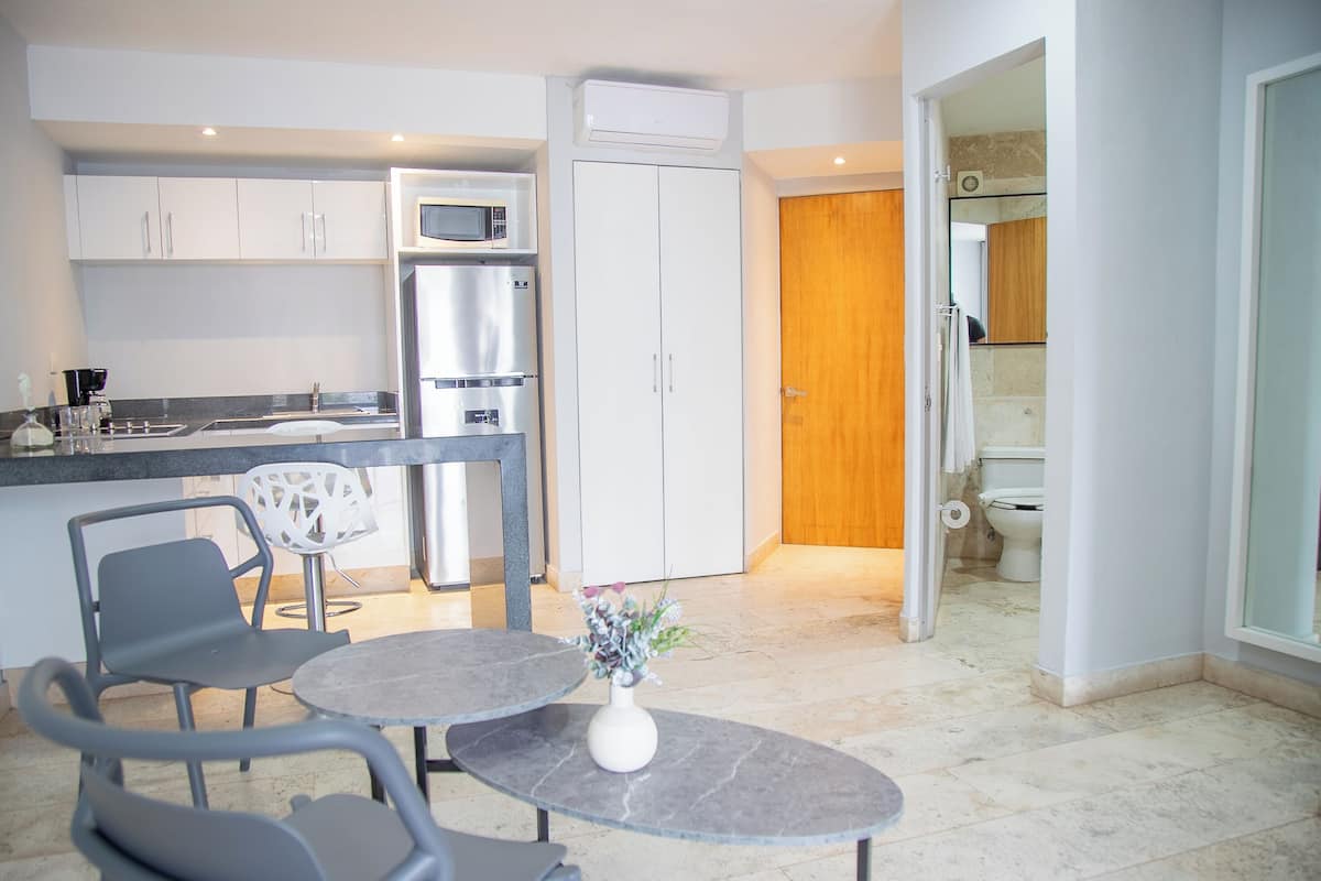 A modern kitchen with a dining area, a refrigerator, a microwave, and a wooden door leading to a bathroom.