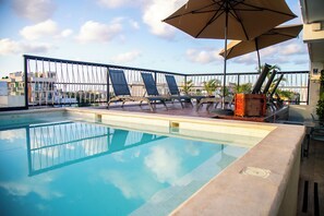 A swimming pool with lounge chairs and umbrellas, surrounded by a fence and buildings in the background. - Hotelito del Mar Playa del Carmen (Playa del Carmen)