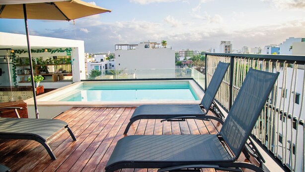 Ein Pool auf dem Dach mit Holzterrasse, Liegestühlen und Blick auf die Stadtlandschaft.