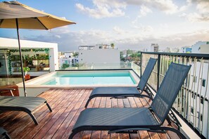 Ein Pool auf dem Dach mit Holzterrasse, Liegestühlen und Blick auf die Stadtlandschaft.