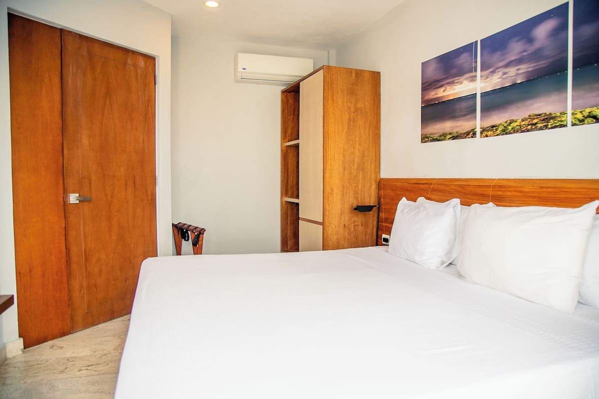 A bedroom with a large bed, wooden wardrobe, and a wall-mounted air conditioner.
