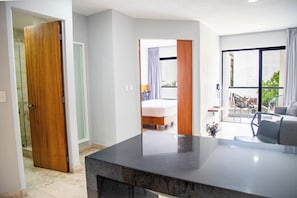 A modern hotel room with a marble countertop, a bed with a wooden headboard, a balcony with chairs, and a large window.