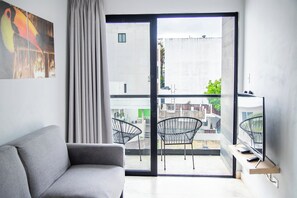 A modern living room with a grey sofa, a large window with a view of the city, and a balcony with two chairs. - Hotelito del Mar Playa del Carmen (Playa del Carmen)