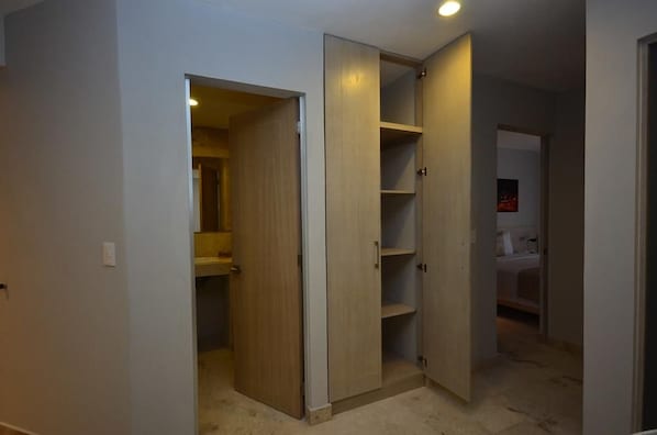 A room with a wooden wardrobe, a bathroom with a white sink, and a door leading to another room.