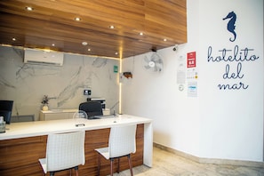 A hotel reception desk with a wooden ceiling, marble walls, and a seahorse logo.