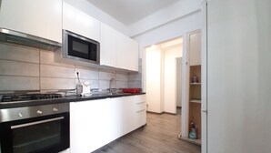 A modern kitchen with white cabinets, a stainless steel stove, a microwave, and a red cutting board. - Central Apartment Bucharest (București)