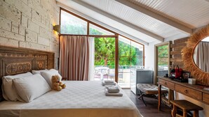 Quarto com cama grande, escrivaninha de madeira, cadeira, cômoda e grande janela com vista para árvores.
