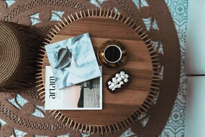 Uma mesa de madeira redonda com uma revista, uma chávena de café e um cesto de malhames.