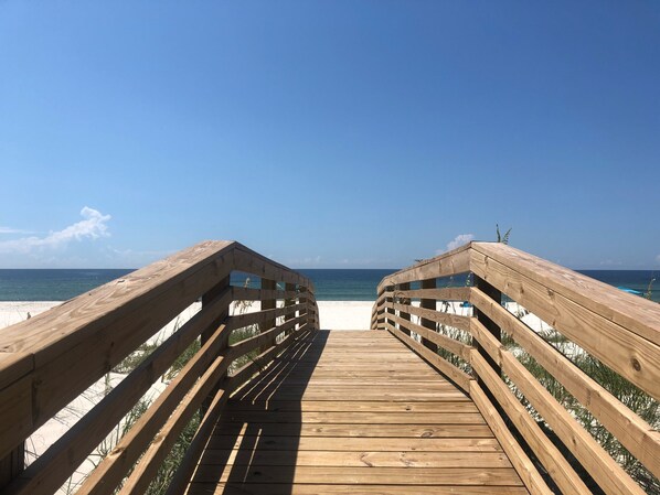 Um calçadão de madeira que leva a uma praia, com céu claro.