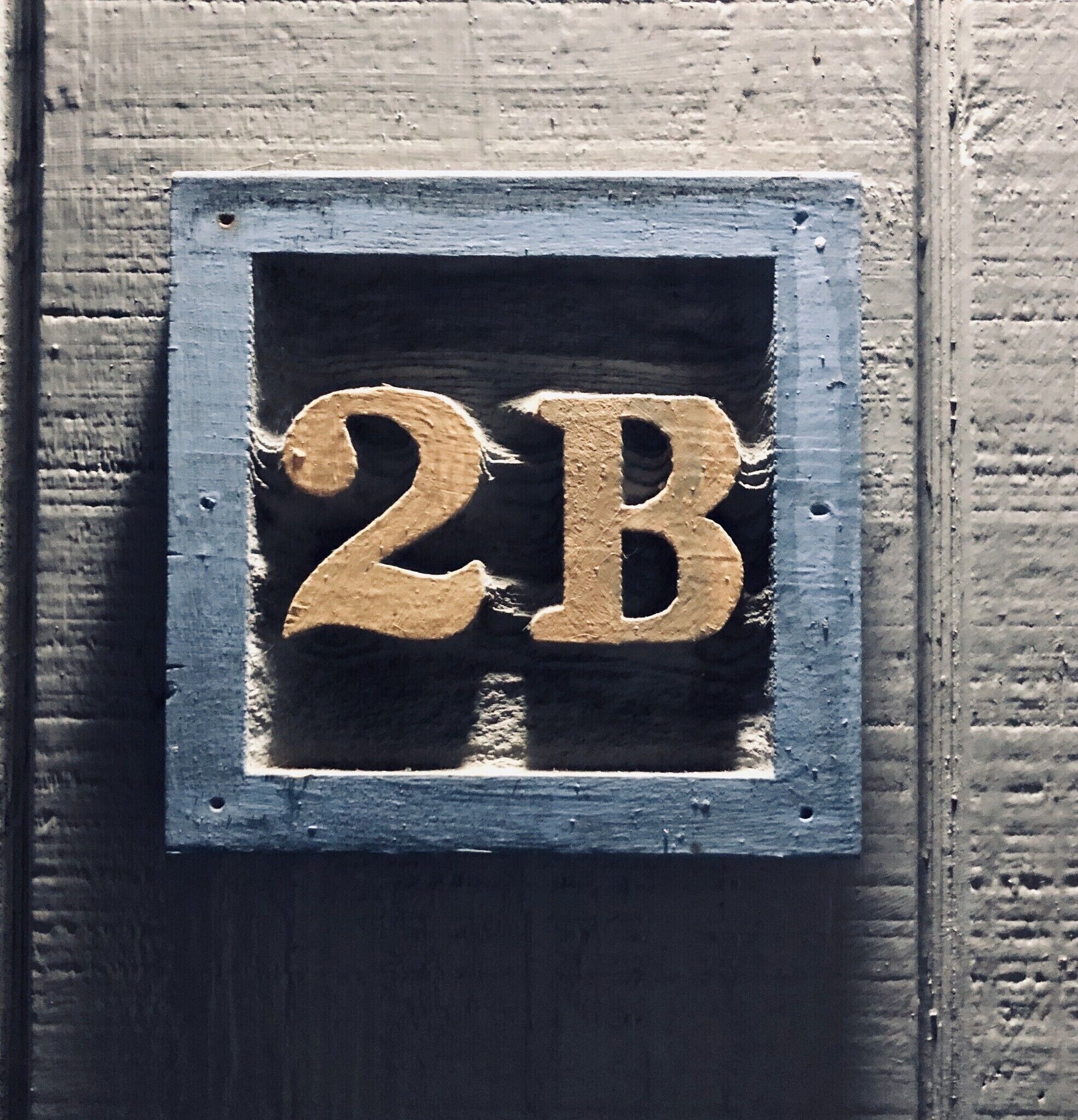Ett husnummer, ’2B’, i en rustik, väderbiten metallram.
