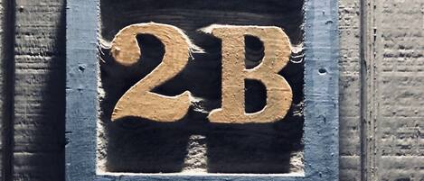Ett husnummer, ’2B’, i en rustik, väderbiten metallram.