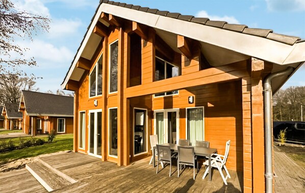 A two-story wooden house with a covered patio, large windows, and a dining area with outdoor furniture. - Gorgeous home in HEEL with WiFi (HEEL)