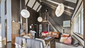 Un salon spacieux doté d’une cheminée, de poutres en bois, d’un escalier et d’une grande fenêtre.