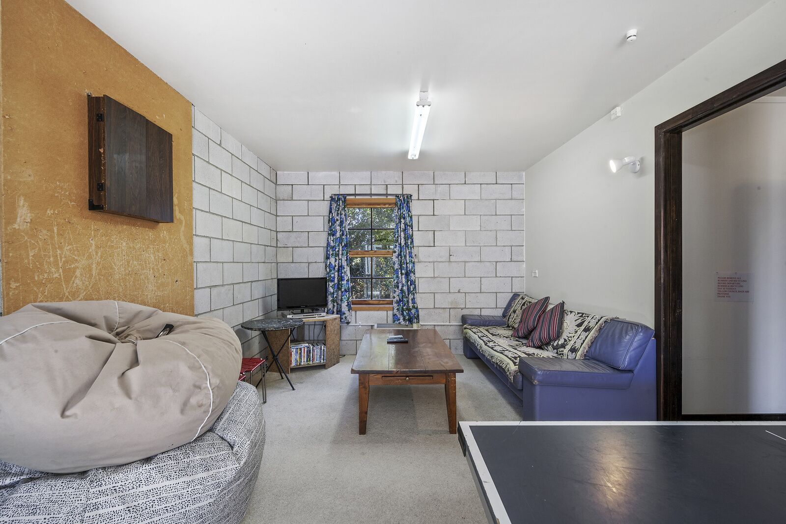 A living room with a sofa, a bean bag, a coffee table, a TV, and a ping pong table.