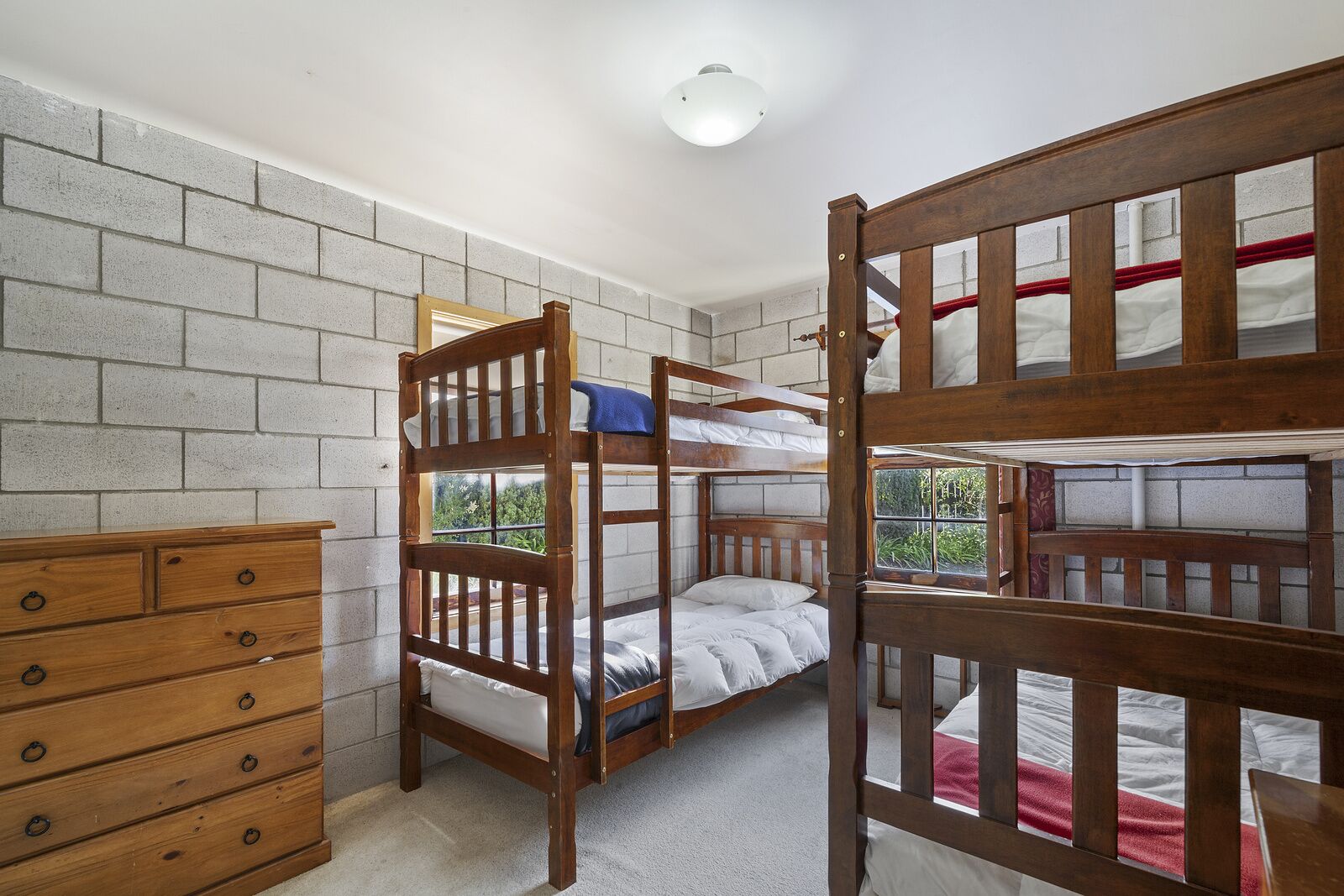 A room with bunk beds, a wooden dresser, and a window with a view of greenery.