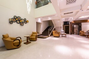 Um hall amplo com teto alto, escada e um objeto decorativo fixado na parede.